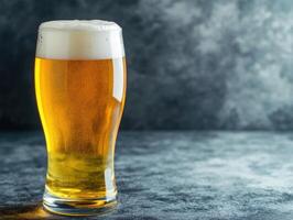 Golden beer served in a glass against a textured gray background photo