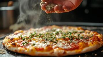Cook adding spices to freshly baked pizza with herbs, mozzarella cheese and tomato sauce photo