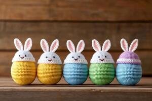 Five colorful crochet easter eggs wearing bunny hats sitting on rustic wooden surface photo