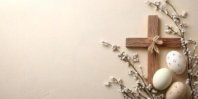 Easter eggs and wooden cross with willow branches lying on beige background photo