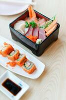 Sashimi and sushi rolls served with soy sauce on wooden table photo