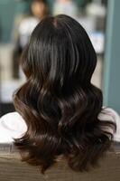 Glossy wavy black hair styled in soft curls, viewed from back in salon setting photo