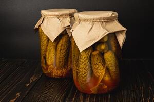 Homemade canned pickles and peppers in jars on a rustic wooden table photo