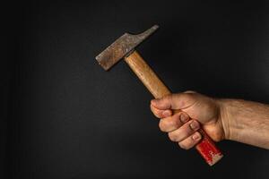 Hand holding a hammer against a dark background photo