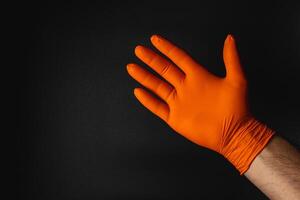 Hand in an orange glove displayed against a dark backdrop photo