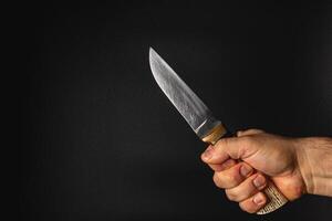 Hand holding a sharp knife against a dark background photo