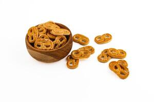 Crunchy pretzels served in a wooden bowl with some scattered on a white surface photo