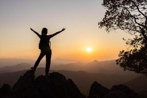 Silhouette of A person standing on top of the mountain with their arms raised in victory, overlooking misty mountains and clouds at sunrise. photo
