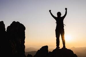 Silhouette of A person standing on top of the mountain with their arms raised in victory, overlooking misty mountains. photo
