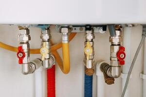 Close-up view of water heater pipes and valves in utility room, featuring colorful connectors and tubes. Essential components for heating system maintenance and operation. Gas boiler taps. photo