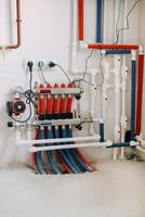Central heating system image showing multiple red and blue pipes connected to control panel with valves and gauges. System is set up against plain wall. photo