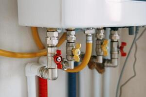 Close-up view of water heater pipes and valves in a utility room, featuring colorful connectors and tubes. Essential components for heating system maintenance and operation. Gas boiler taps photo