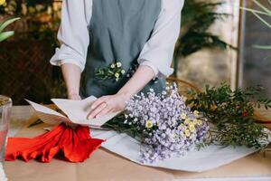 florist works on preparing beautiful floral arrangement. Various flowers and materials lie on table, emphasizing the artistic and inspiring atmosphere associated with floral design and presentation. photo