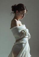 Woman stands with eyes closed, wrapped in white fabric. Her expression is peaceful and contemplative. The pose and drapery evoke a sense of elegance and grace. photo