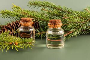 Two glass bottles with a cork with natural oil against the background of a green spruce branch with a cone. Front view. An alternative to medicine. photo