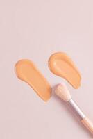 Two cosmetic strokes of natural tone liquid foundation powder on a beige vertical background with a makeup brush. top view. copy space. texture sample photo