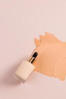 Cosmetic bottle with dropper with natural foundation powder on a sample texture of liquid smeared powder in beige tone. vertical top view. copy space photo