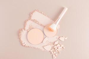 Three gorgeous strokes and a round block of compact powder in a natural tone on a beige background, a makeup brush, pieces of broken powder. top view photo