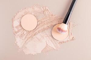 Two round blocks of compact powder in a natural tone lie on a sample of scattered powder with a makeup brush. cosmetic background. texture sample. photo