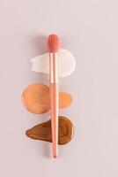Three gorgeous strokes of liquid foundation in various tones on a beige vertical background with a professional makeup brush lying on them. top view photo