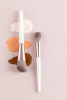 A beautiful cosmetic background with texture samples of liquid foundation powder in different tones and two makeup brushes. vertical top view. layout. photo