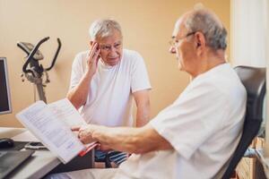 Patient is having exam at cardiologist. Doctor is looking at his medical files. Patient is complaining about pain. photo