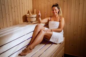 Happy woman enjoys a private sauna at a high-end spa. She is looking at camera, smiling and showing thumbs up. photo