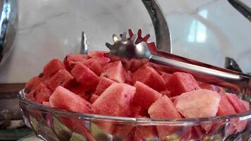 Fresh watermelon served in a clear bowl with metal tongs video