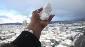 Snow falls over city landscape as hand holds freshly gathered snow video