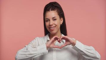 Smiling black woman making heart gesture on pink background video