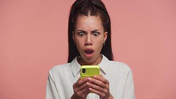 Shocked woman reading unexpected message on phone on pink background video