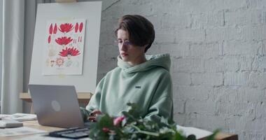 A woman in a green sweatshirt is working on her laptop video