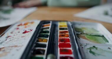 Close-up of open partially used watercolor paints standing on the artist's desk, while he is working on paintings in the studio video