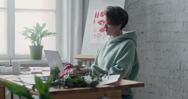 A woman in a green sweatshirt is sitting at a desk with a laptop video