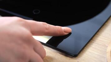 Close-up of a finger turning on a black glass induction cooktop by touching the control area, reflecting light and touch gesture in a modern kitchen setup video