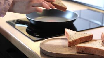 Hand placing triangular sandwich slices into a frying pan on a black induction cooktop, capturing a calm breakfast moment in a bright modern kitchen video