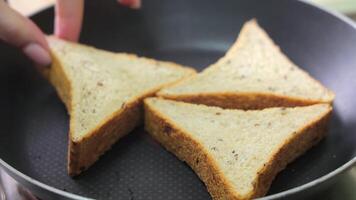 Three triangular sandwich slices placed in a non-stick frying pan, close-up view shows hand adjusting the pieces for even toasting and heat contact video