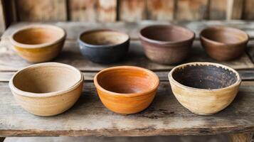 Earthy ceramic bowls displayed on rustic wooden table, showcasing various shapes and colors. warm tones evoke sense of craftsmanship and natural beauty photo
