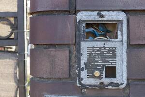 Old Damaged Intercom with Exposed Wires on Brick Wall photo