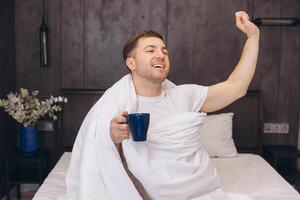 Man Waking Up and Stretching in Bed While Holding a Coffee Mug photo