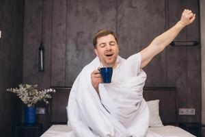 Man Waking Up and Stretching in Bed While Drinking Coffee photo