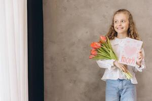 Smiling girl holding tulips and handmade postcard for Mother's Day photo