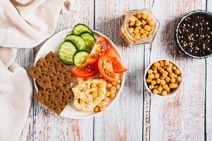 Hummus, chickpeas, tomato, cucumber, grain crackers on a plate on the table top view photo