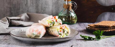 Spring rolls in rice paper with crab sticks, cucumber, greens and sauce on a plate on web banner photo