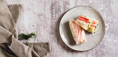 Spring rolls with crab meat, cucumber and herbs on a plate on the table top view web banner photo