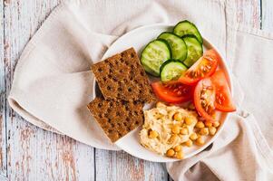 Close up of platte with hummus, chickpeas, tomato, cucumber and grain crackers on a plate top view photo