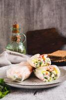 Spring rolls in rice paper with crab sticks, cucumber, greens and sauce on a plate on vertical view photo