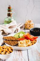Hummus, chickpeas, tomato, cucumber, grain crackers on a plate on the table vertical view photo