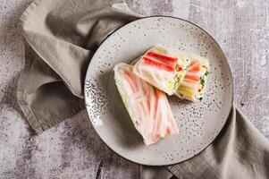 Close up of spring rolls in rice paper with crab sticks, cucumber, greens and sauce on on top view photo