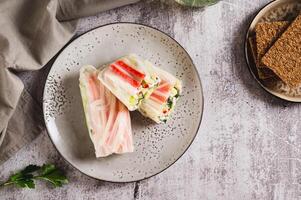 Spring rolls in rice paper with crab sticks, cucumber, greens and sauce on a plate on top view photo